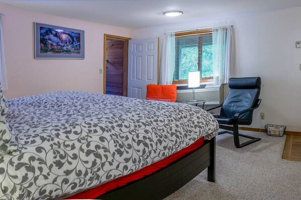 Ein Schlafzimmer mit einem Bett, einem Sessel, einem Fenster mit Jalousien und einer Tür.