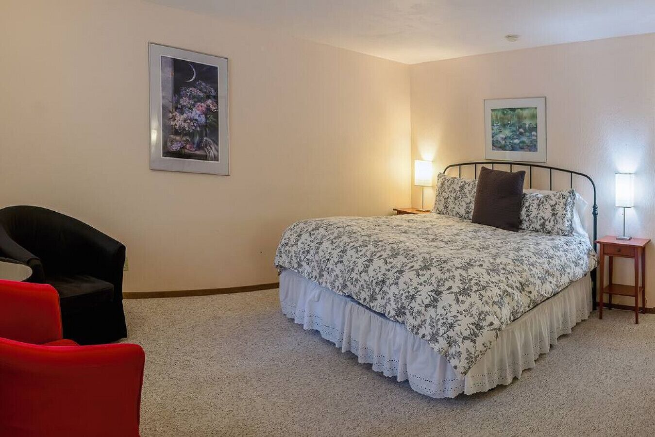 A bedroom with a bed, two bedside tables with lamps, a chair, and two framed pictures on the wall.