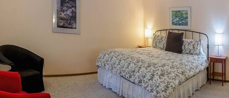 A bedroom with a bed, two bedside tables with lamps, a chair, and two framed pictures on the wall.