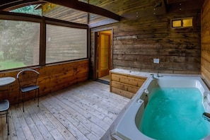 Enjoy a peaceful retreat with a view of the outdoors from the large window, a hot tub, and a deck area.