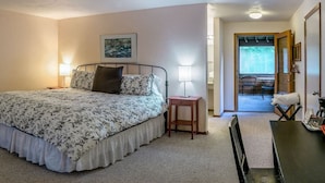 Une chambre avec un lit, des lampes de chevet, une petite table et une chaise. Une porte donne accès à un balcon équipé d’un coin salon extérieur.