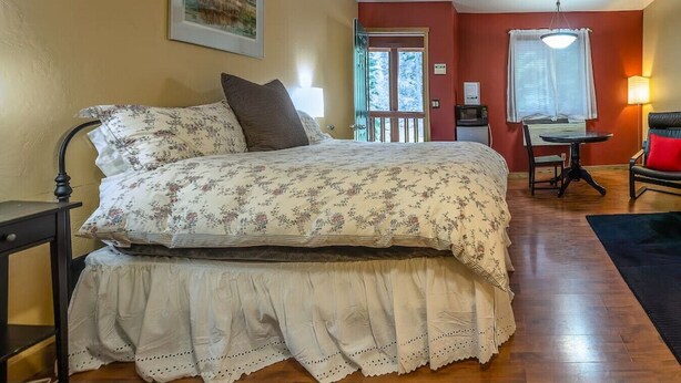 A bedroom with a bed, a desk, a chair, a lamp, and a window with curtains. - Lodge Room 5 with Jacuzzi Tub at Green Springs Inn (Ashland)