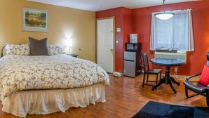 A bedroom with a bed, a desk, a chair, a refrigerator, and a window with curtains. - Lodge Room 5 with Jacuzzi Tub at Green Springs Inn (Ashland)