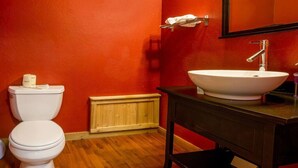 A bathroom with a white toilet, a wooden floor, a white sink, and a red wall. - Lodge Room 5 with Jacuzzi Tub at Green Springs Inn (Ashland)