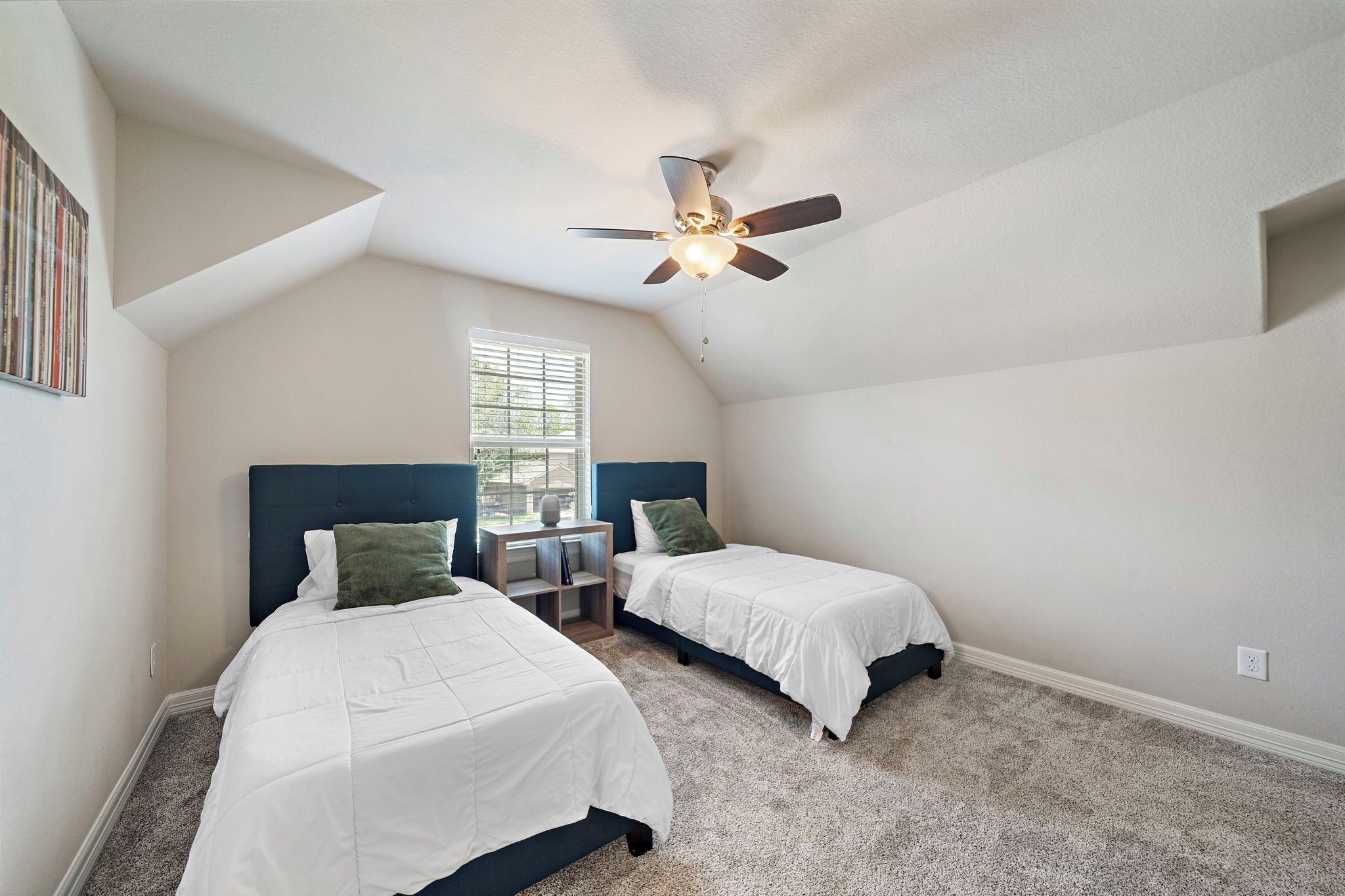 A bedroom with two beds, a ceiling fan, a window, and a small table.