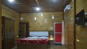 A wooden-paneled room with a bed, a red door, and an air conditioning unit. - De Aloha Resort (Tezpur)