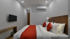 A modern hotel room with a bed, a TV mounted on the wall, and an air conditioning unit above the bed. - Hotel Emporio (Ghaziabad)