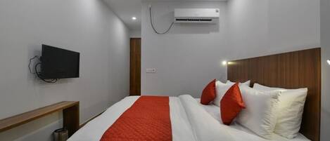 Una habitación de hotel moderna con una cama, un televisor montado en la pared y un equipo de aire acondicionado sobre la cama.