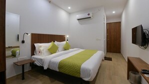 A hotel room with a bed, bedside table, wall-mounted TV, air conditioning unit, and a wooden door. - Hotel Emporio (Ghaziabad)