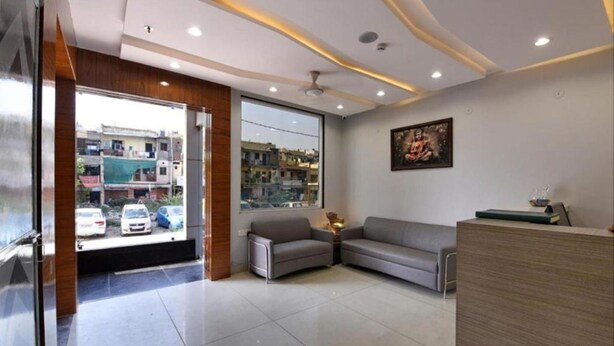 A reception area with a sofa, a desk, and a large window offering a view of the street. - Hotel Emporio (Ghaziabad)
