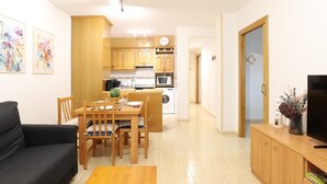 A compact living space with a dining area, a sofa, a TV, and a kitchen with wooden cabinets and a microwave.