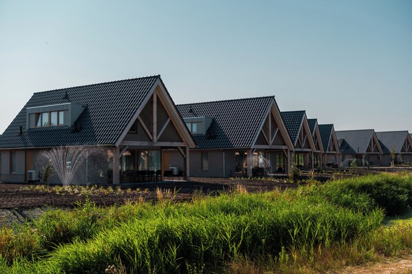 A row of modern, multi-story houses with pitched roofs and large windows, set in a landscaped area with dense greenery. - EuroParcs Cadzand (Cadzand-Bad)