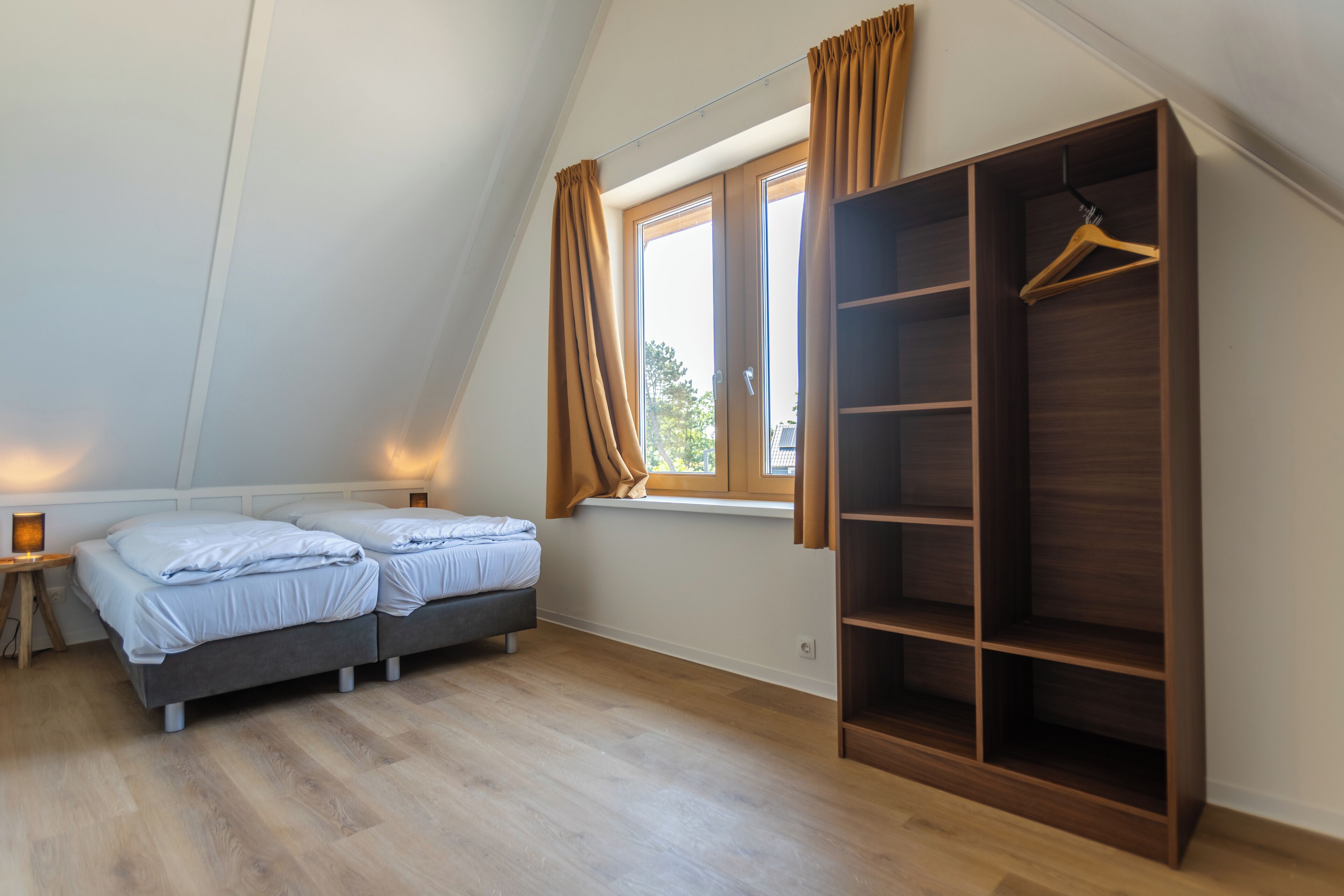 Ein Schlafzimmer mit zwei Betten, einem Holzschrank, einem Fenster mit Vorhängen und einem Nachttisch mit Lampe.