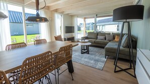 A spacious living area with a wooden dining table, wicker chairs, a sofa, and a floor lamp. - EuroParcs Cadzand (Cadzand-Bad)