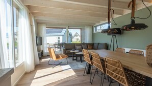 A spacious living area with a wooden dining table, wicker chairs, a sofa, and a television. - EuroParcs Cadzand (Cadzand-Bad)