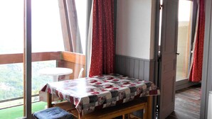 Ein Zimmer mit einer hölzernen Bank, einem Tisch mit einer Patchworkdecke und Blick auf Grünfläche.