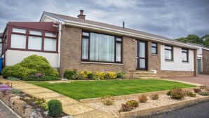 A two-story house with a front lawn, a driveway, and a garden area with various plants. - Spacious family cottage close to the beach and just a short drive from Edinburgh (Limekilns)