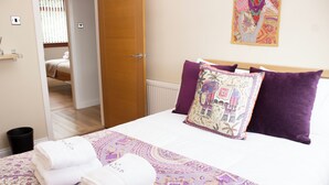 A neatly made bed with a patterned bedspread, two purple pillows, and two rolled towels on the bed. - Spacious family cottage close to the beach and just a short drive from Edinburgh (Limekilns)