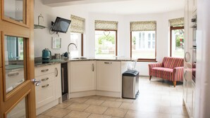 A kitchen with white cabinets, a built-in oven, and a coffee maker. There is a window with a heart-shaped decoration and a striped chair in the background. - Spacious family cottage close to the beach and just a short drive from Edinburgh (Limekilns)