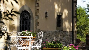 A stone building with a wrought iron table and chairs, potted plants, and a window with a metal gate.