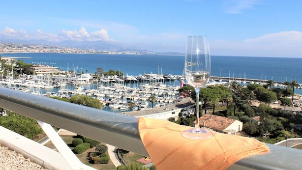 Ein Yachthafen mit Booten, ein Glas Wein auf einem Balkon und eine Küstenstadt im Hintergrund.