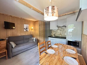 Eine moderne Küche mit Holztisch gedeckt zum Essen, einem grauen Sofa und einem an der Wand befestigten Fernseher.