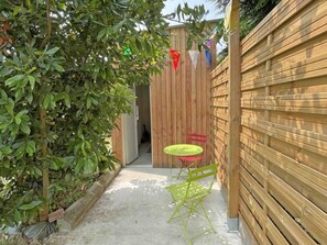 Un estrecho sendero al aire libre que lleva a una puerta de madera, bordeado por una cerca de madera y una silla verde.