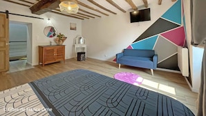 A modern living room with exposed wooden beams, a blue sofa, a TV, and a geometric wall design. - Old house - 8 guests (Réveillon)