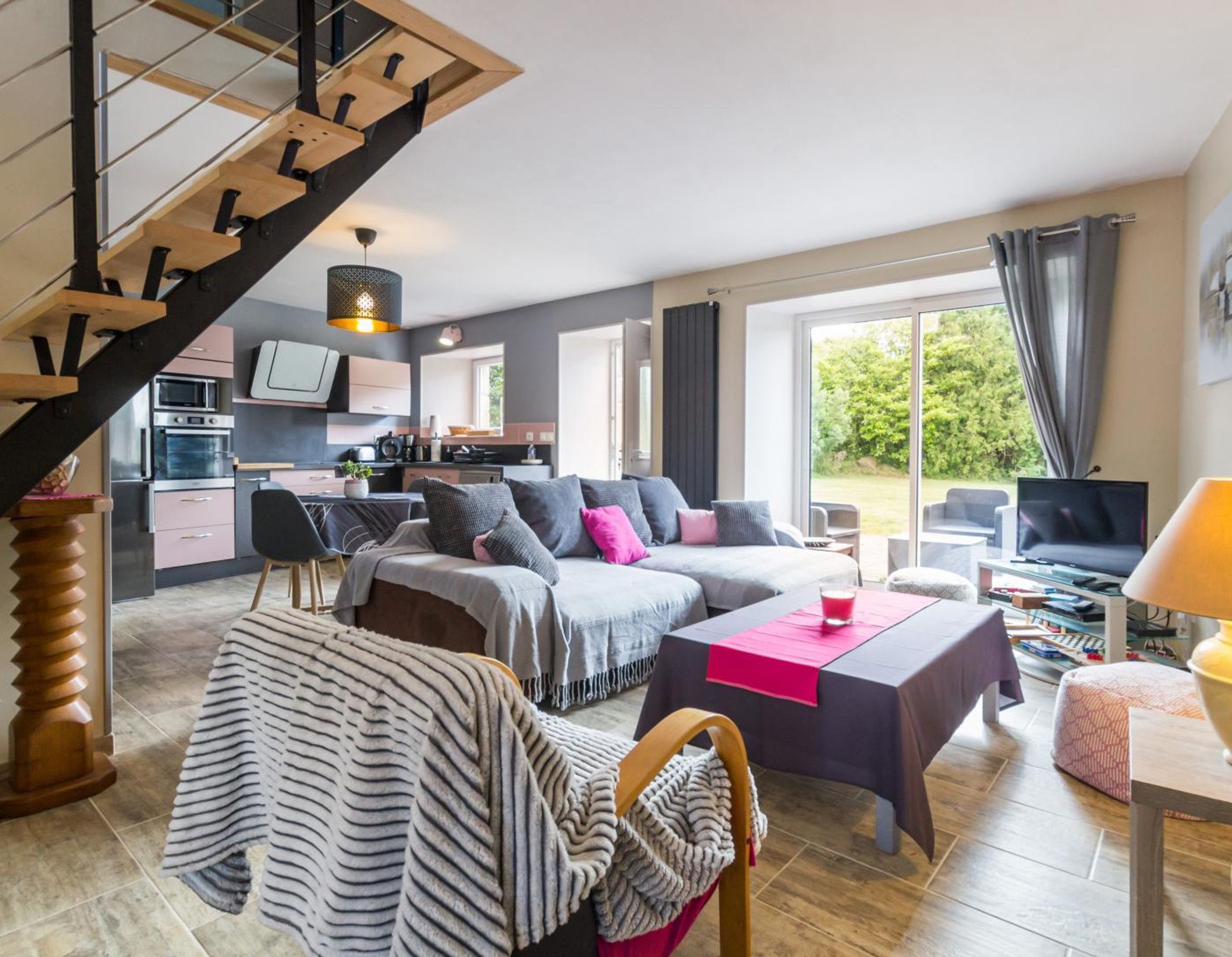 Una sala de estar moderna con un sofá, una mesa de centro y un televisor. Se ve una escalera que lleva a una zona de cocina con microondas y horno.