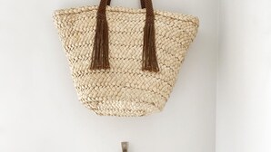 A woven bag with tassels hanging on a wall.