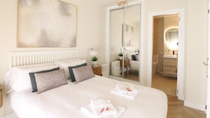 A hotel room with a bed, a ceiling fan, a large abstract painting, a mirror, and a bathroom visible through an open door.