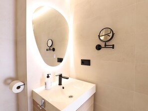 A bathroom with a vanity, two wall-mounted mirrors, a toilet paper holder, and a soap dispenser.