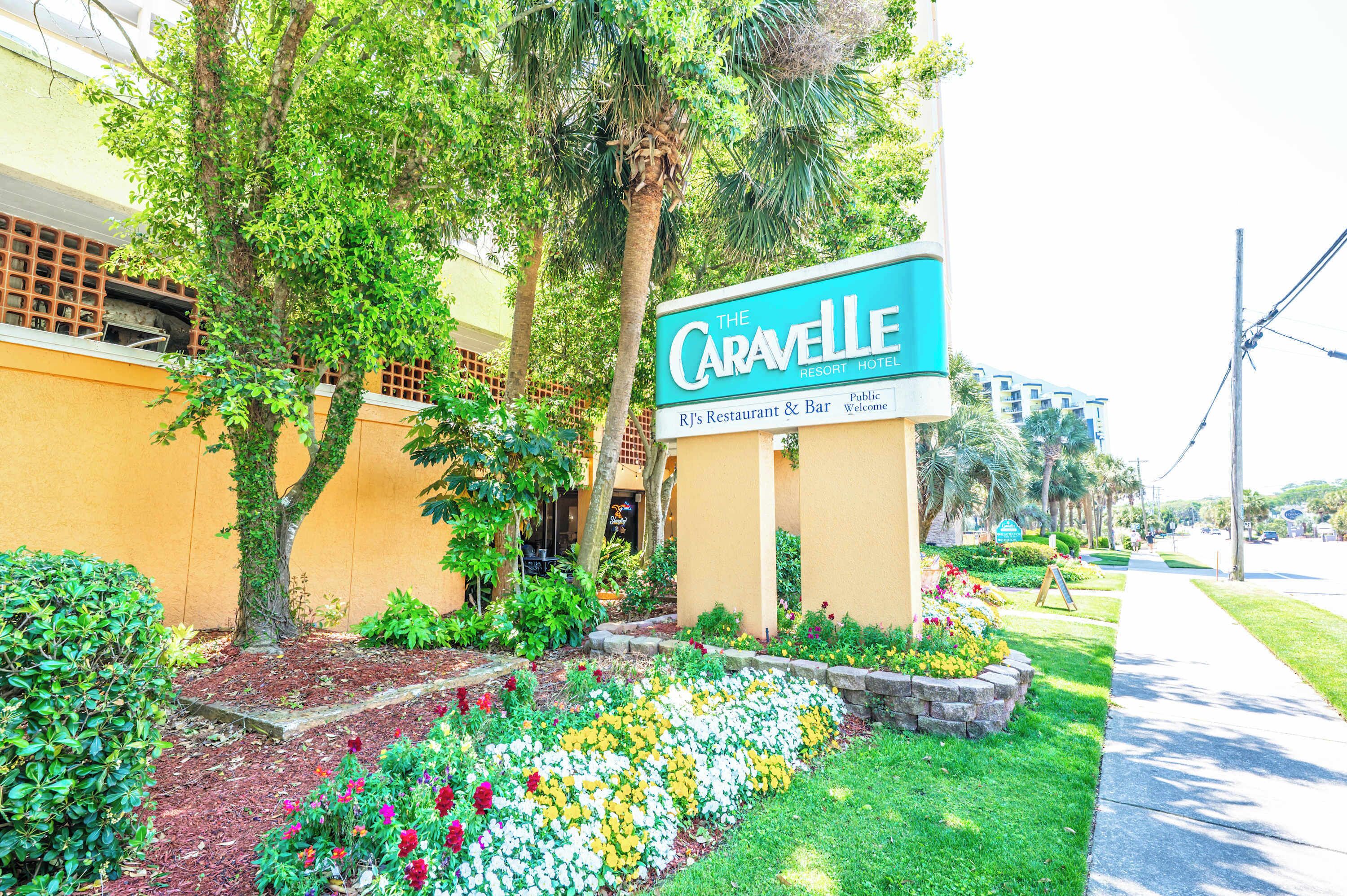 A hotel sign, a landscaped garden with flowers, and a sidewalk.