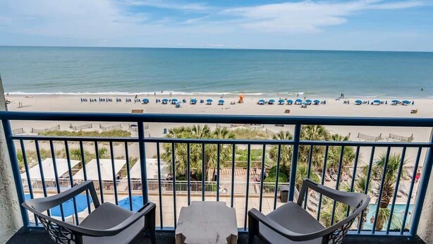 A balcony with a view of a beach and pool area.