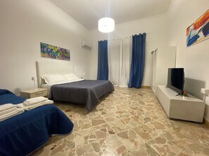 A hotel room with two beds, a flat-screen TV, a painting on the wall, and a stone-patterned floor. - Giachery apartament  (Palermo)