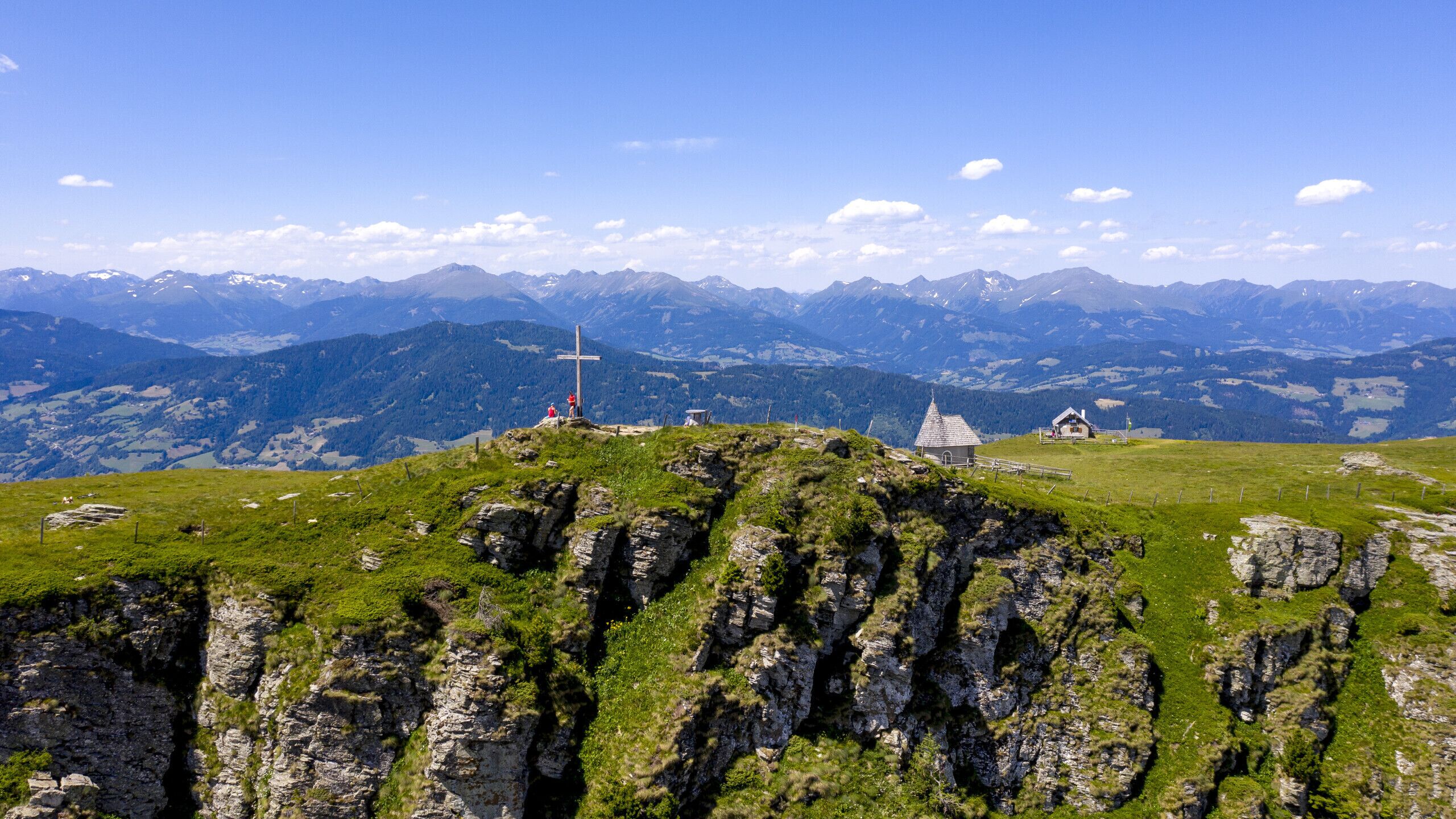 Paesaggio montuoso con una piccola cappella e una croce su una collinetta erbosa.