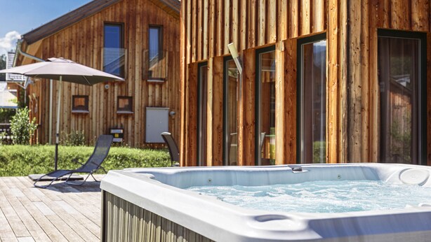 A wooden cabin with a hot tub, a lounge chair, and a patio umbrella. - Premium Chalet # 10 with IR-sauna & whirpool (Murau)
