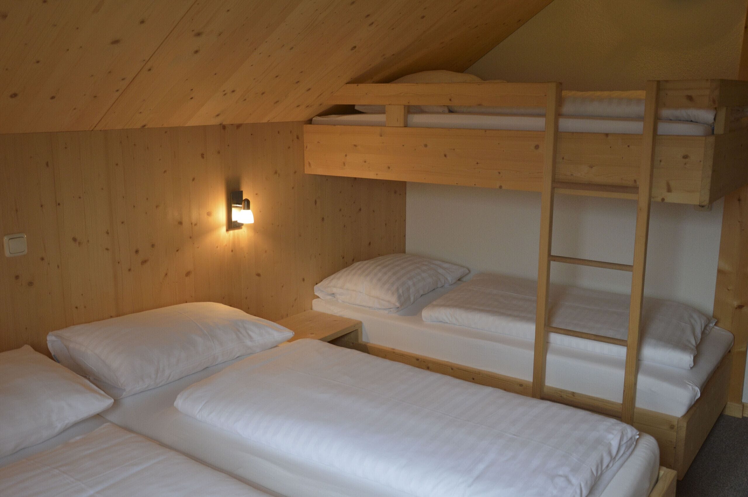 A bunk bed room with wooden walls and a single bedside table with a light fixture.