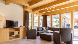 A wooden interior with a TV, sofa, and ottoman, large windows, and a wooden ceiling. - Premium Chalet # 10 with IR-sauna & whirpool (Murau)