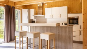 A modern kitchen with wooden walls, a central island with stools, and built-in appliances. - Premium Chalet # 10 with IR-sauna & whirpool (Murau)