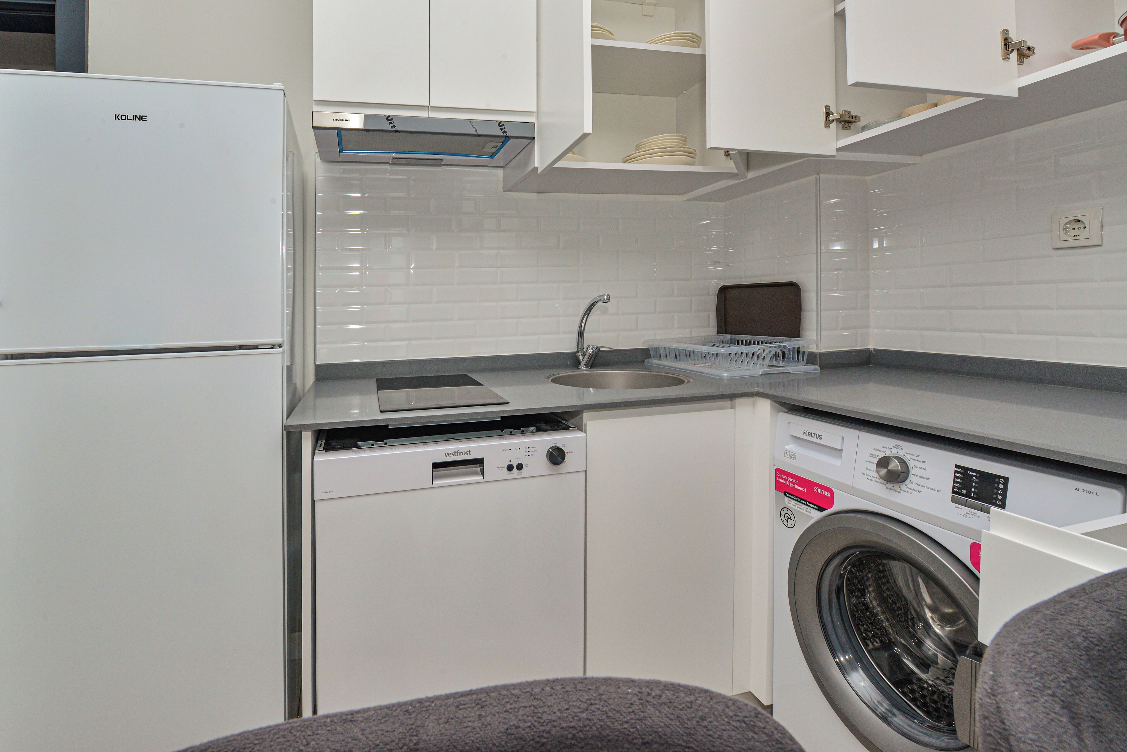 A compact kitchen with a built-in dishwasher, a washing machine, and a sink.