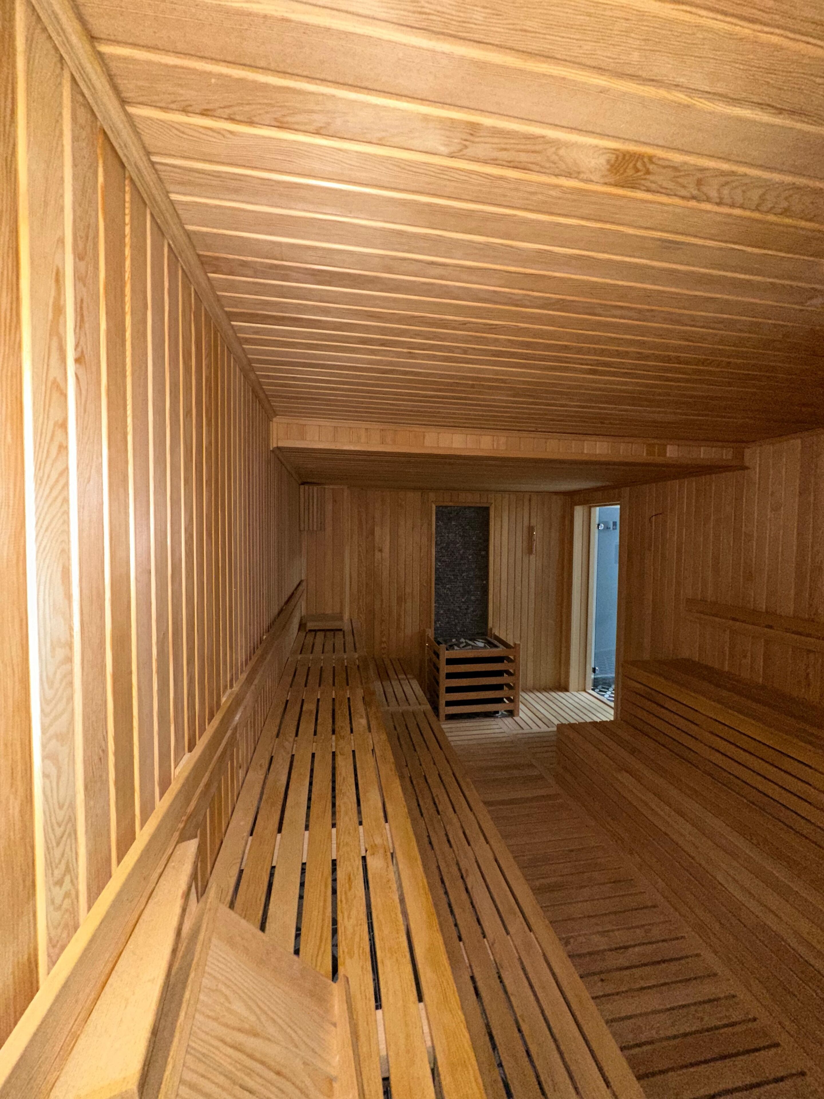 A wooden sauna room with slatted benches and a stone wall.