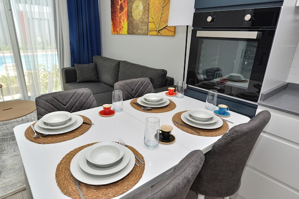 A modern dining area with a white table set for four, grey upholstered chairs, and a kitchen in the background. - C Suites Antalia Airport (Antalya)