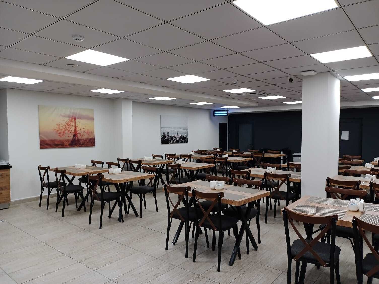 A conference room with multiple tables and chairs, white walls, and ceiling lights.