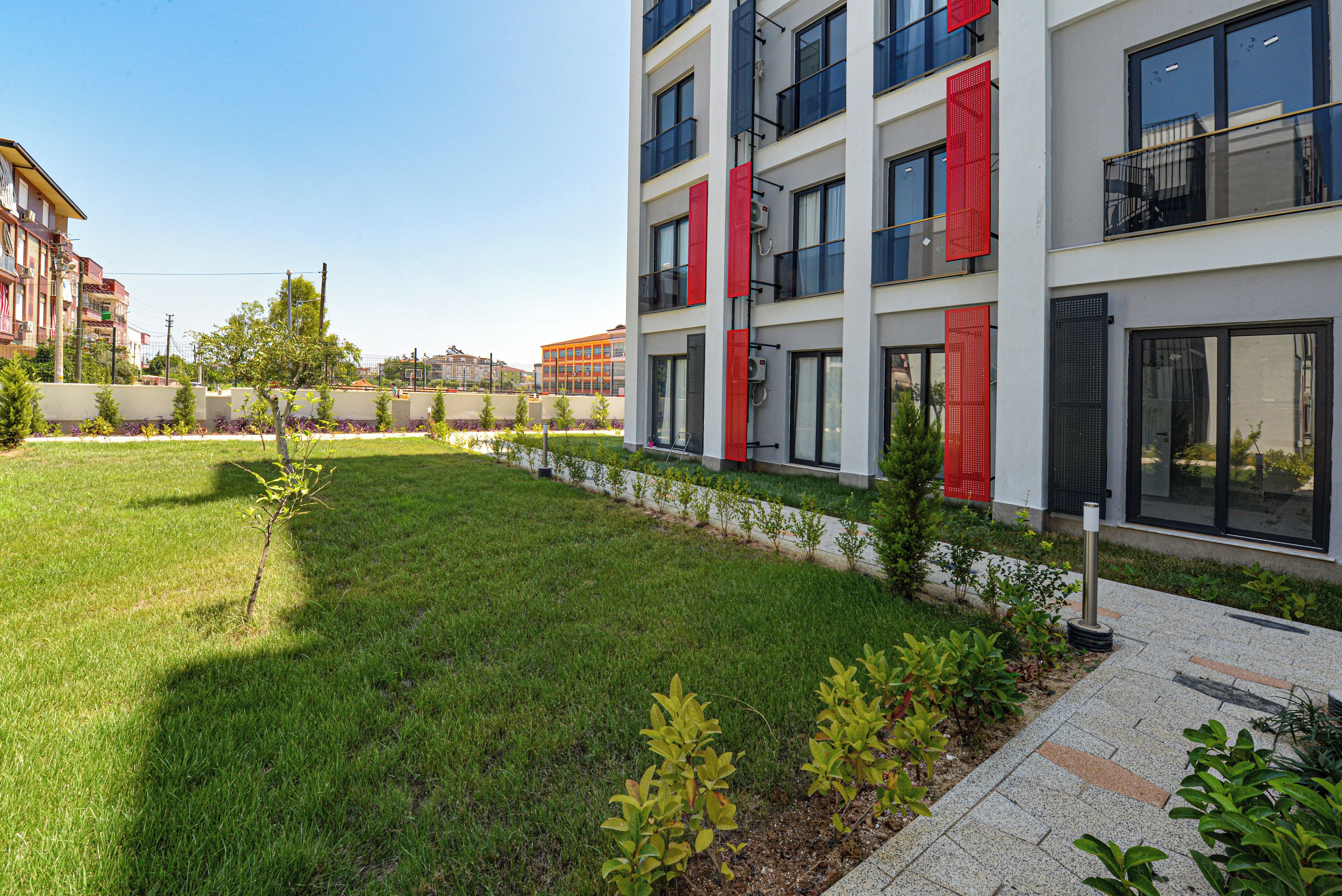 Edifici modern amb balcons i grans finestres, envoltat d'un jardí ben cuidat i petites plantes.