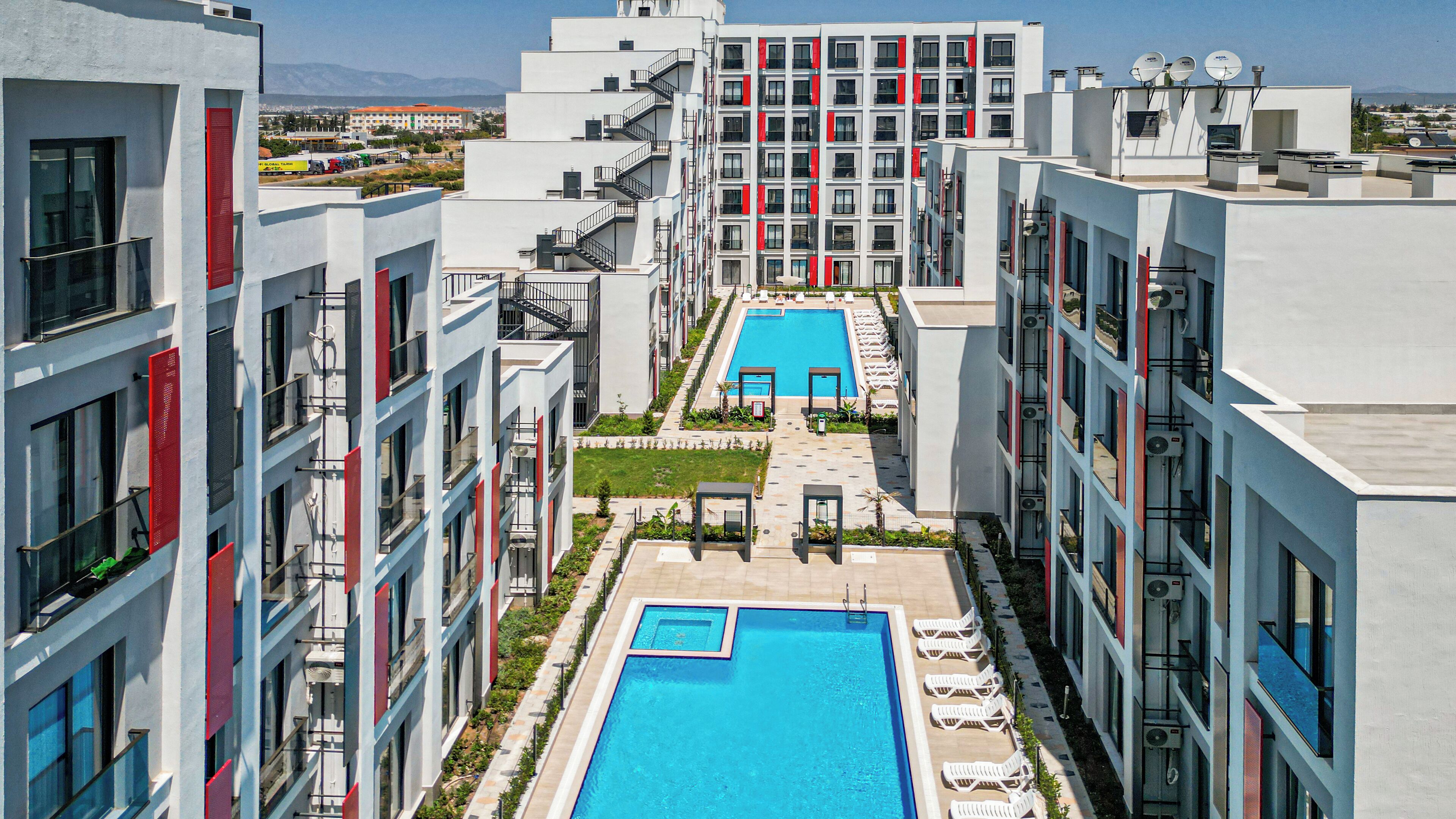 Un moderno edificio de apartamentos con piscina central, balcones y vistas del entorno.