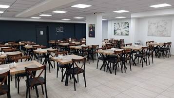 Une salle de conférence spacieuse, dotée de plusieurs tables et chaises, de murs blancs et d’un éclairage au plafond.