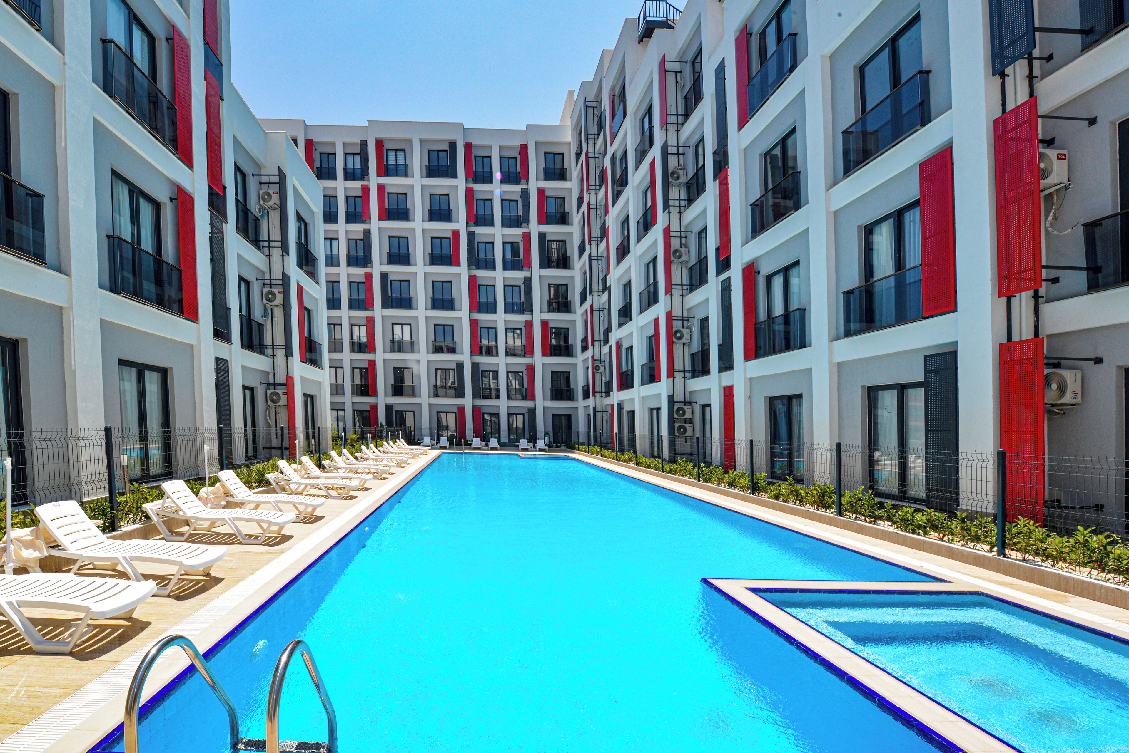 A modern hotel with a central swimming pool, multiple balconies, and sun loungers along the poolside.