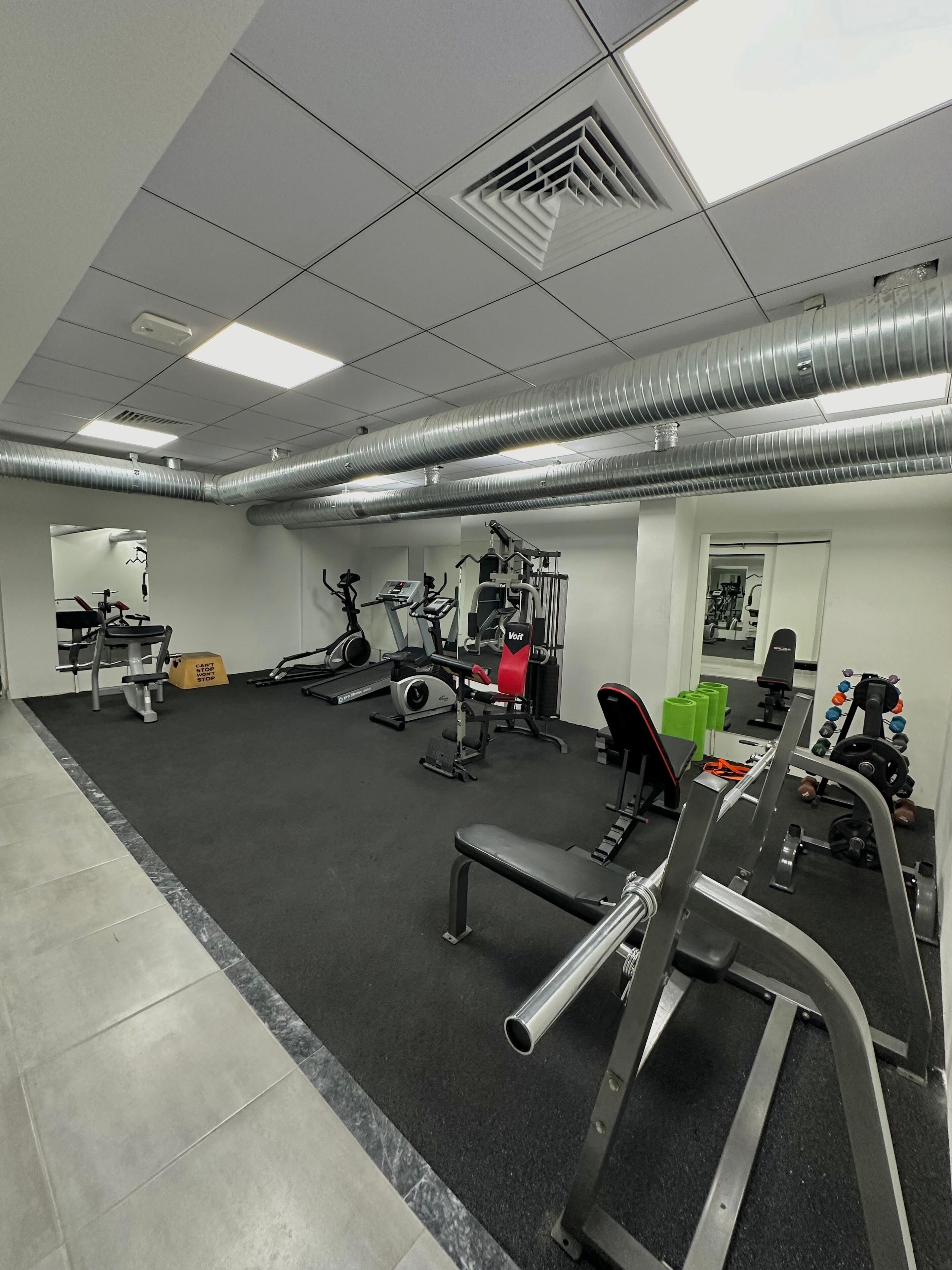 Un gimnasio con varios equipos de ejercicio, incluyendo cintas de correr, máquinas de pesas y pesas sueltas.