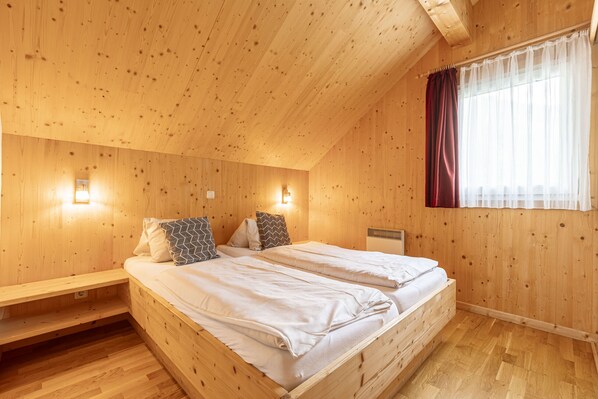 Ein Schlafzimmer einer Holzhütte mit zwei Betten, einer Bank und einem Fenster mit Vorhängen.